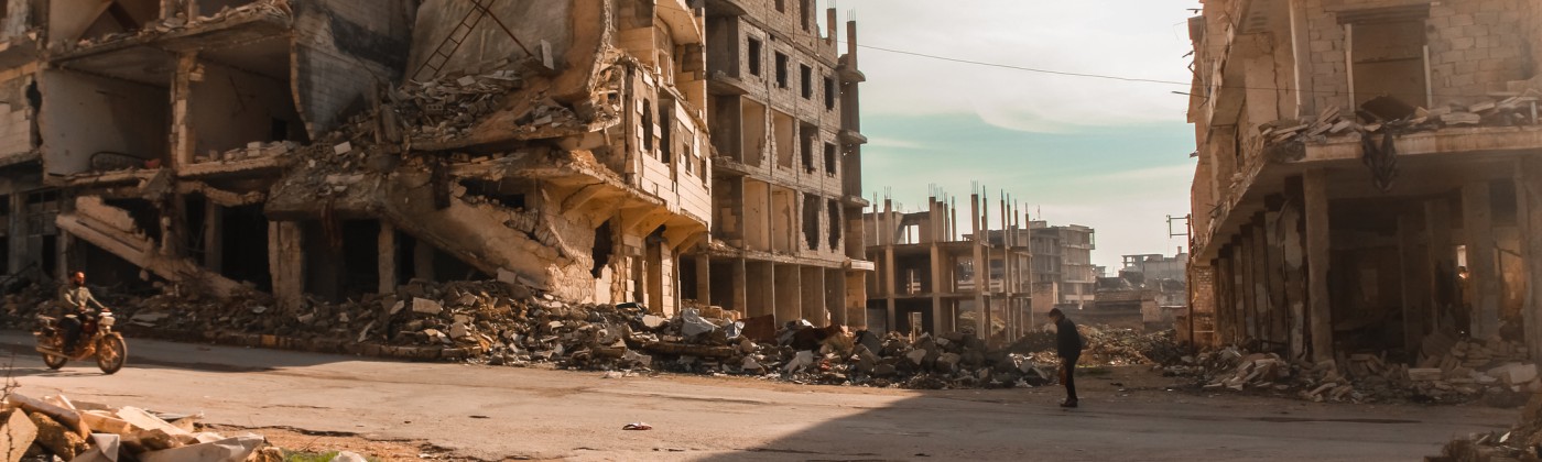 person standing in street lined by bombed buildings