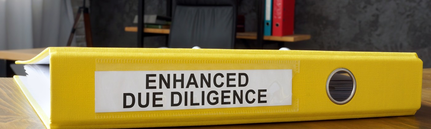 Yellow binder labeled enhanced due diligence resting on a wooden desktop