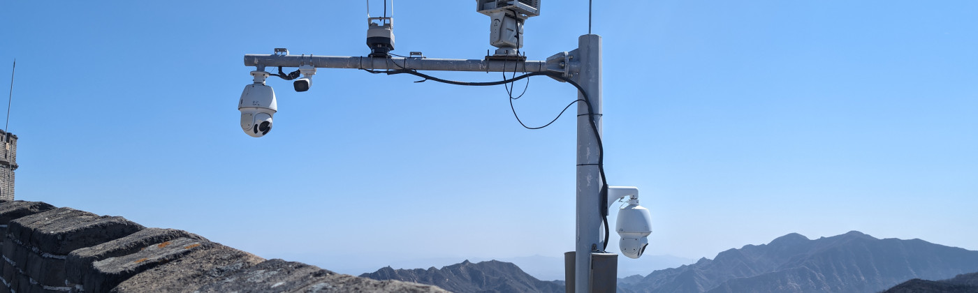 a surveillance camera, mounted on a post, with mountains visible in the background