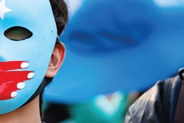 Person with East Turkestan flag face mask with a hand of the People's Repbulic of China flag covering their mouth