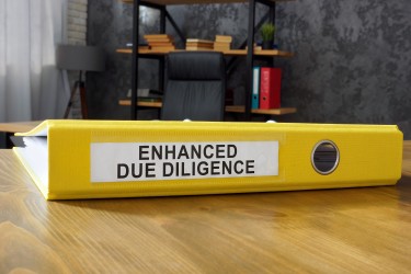 Yellow binder labeled enhanced due diligence resting on a wooden desktop