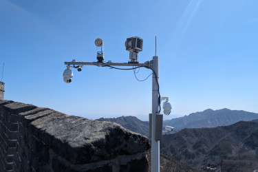 a surveillance camera, mounted on a post, with mountains visible in the background